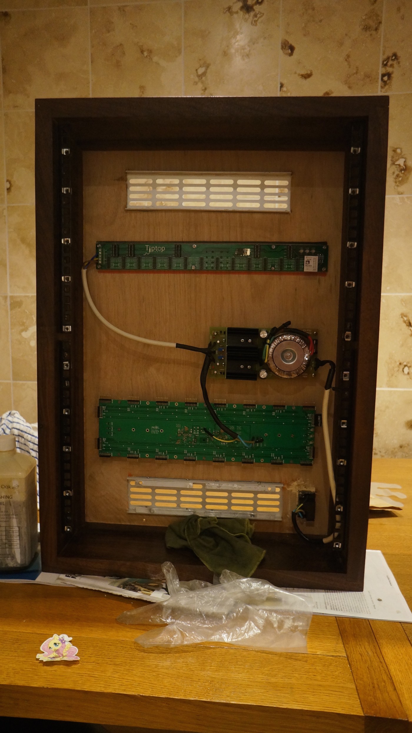 An empty wooden Eurorack case standing on a table, with two Tiptop bus boards and a toroidal-transformer linear power supply mounted inside and ventilation grilles above and below.