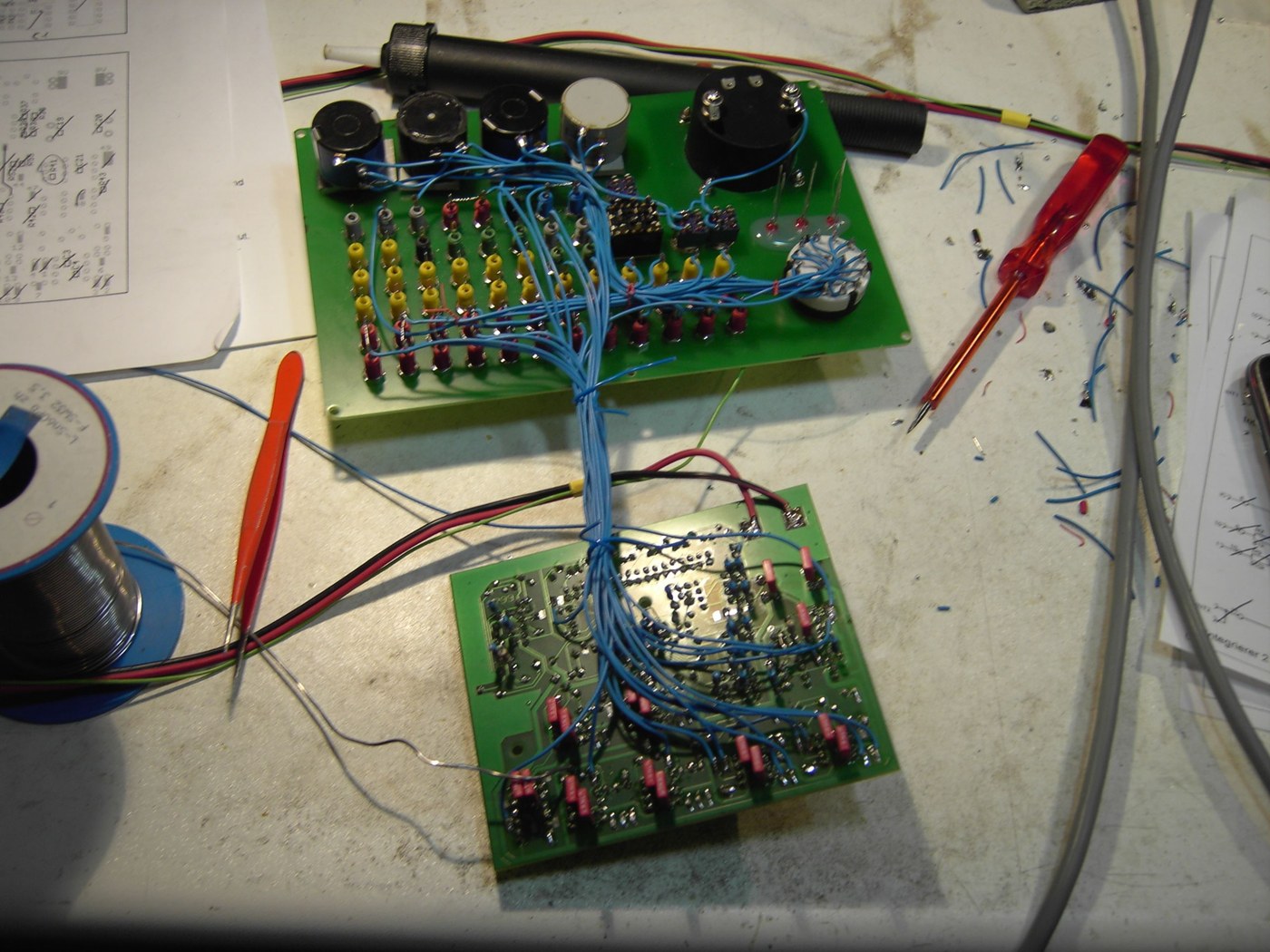 Two circuit boards on a bench during construction, joined by a thick bundle of blue wires: the patch-panel board above with rows of yellow, red and black sockets fitted, and the main board below showing its dense solder side.